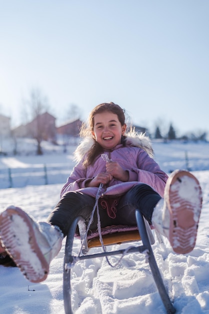 Una niña sonriente paseo en trineo niño feliz jugando en el invierno cubierto de nieve afuera