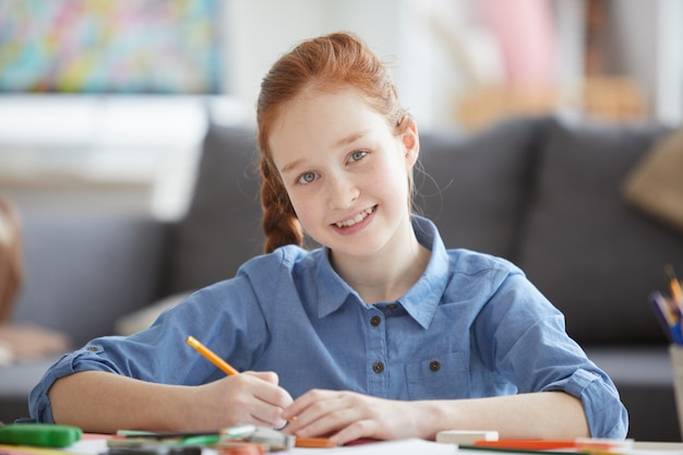 Niña sonriente pelirroja haciendo dibujos