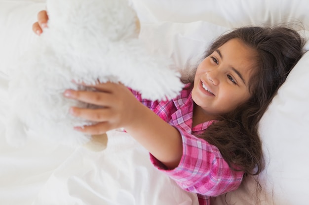 Niña sonriente con peluche descansando en la cama