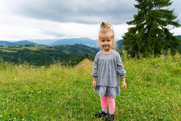 Niña sonriente de pie al aire libre con vistas a las montañas. Tiempo feliz de verano