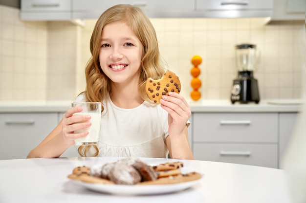 Niña sonriente posando con vaso de leche y galletas en las manos.