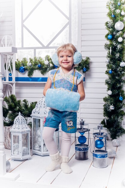 Niña sonriente que se coloca al lado de un árbol de navidad