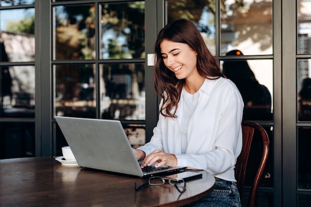 Niña sonriente que trabaja en la computadora portátil en la cafetería