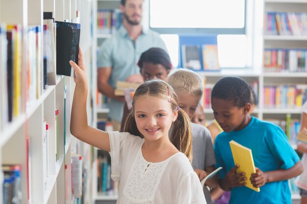 Niña sonriente quitando el libro de la estantería en la biblioteca