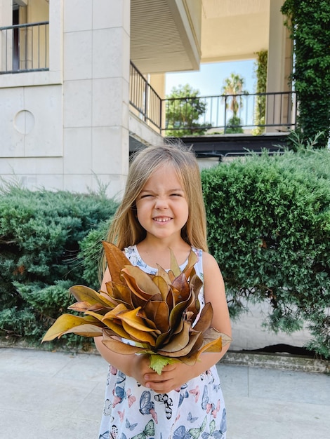 Niña sonriente con un ramo de follaje amarillo se encuentra cerca de la casa