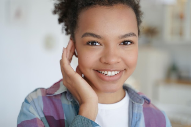 Niña sonriente de raza mixta que usa auriculares modernos para escuchar música o responder a una videollamada en la cabeza