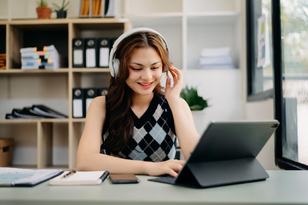 Niña sonriente relajándose en casa, está tocando música usando una computadora portátil con tableta de teléfono inteligente y usando auriculares blancosxA