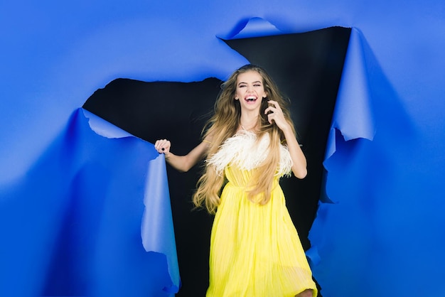 Niña sonriente romper el agujero en papel azul hermosa chica en vestido amarillo pasa a través del agujero en