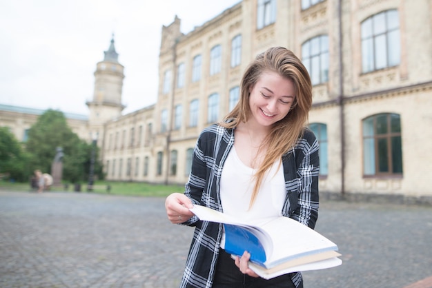 Niña sonriente en ropa casual pasea por el campus y lee un libro.