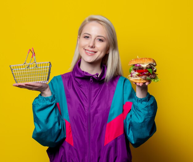 Niña sonriente en ropa de estilo años 80 con canasta de hamburguesas y supermercados