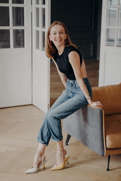 Niña sonriente con ropa informal sentada en un acogedor sofá posando para un retrato en el interior de la casa