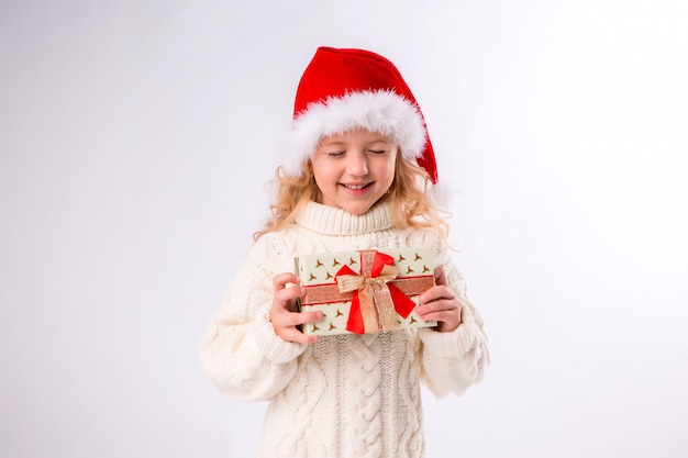 Niña sonriente en santa hat con caja de regalo sobre fondo blanco.