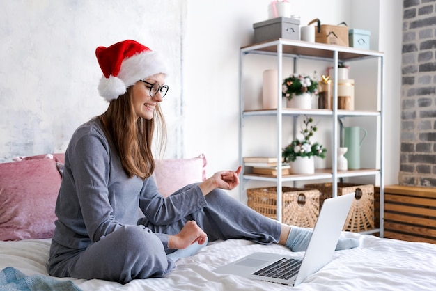 Niña sonriente de Santa con ropa acogedora con sombrero de Navidad usando una computadora portátil