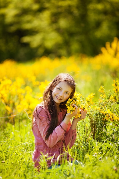 Niña sonriente sentada en el campo de flores amarillas de primavera