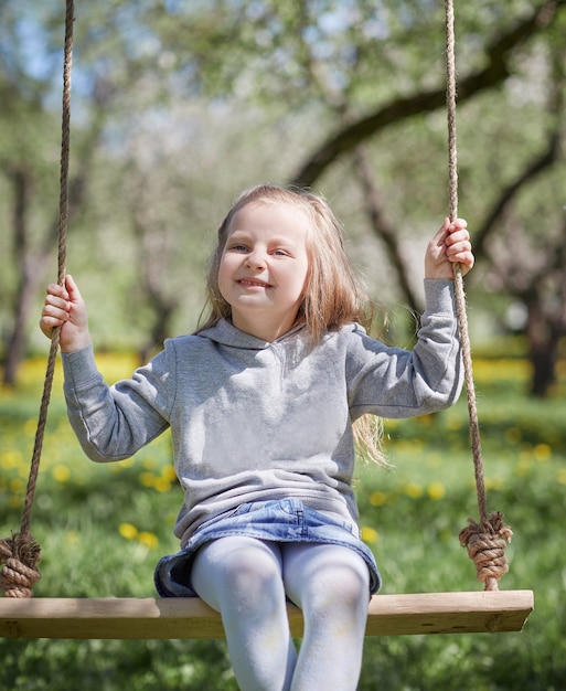 Niña sonriente sentada en un columpio en el jardín. el concepto de felicidad de los niños.