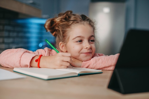 Niña sonriente sentada en el escritorio haciendo la tarea mientras hace educación en línea usando tableta coronavirus sc