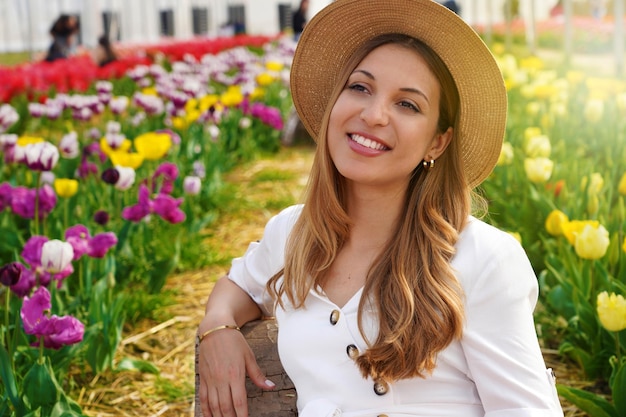 Niña sonriente sentada relajada entre campos de tulipanes al atardecer Mirando hacia un lado