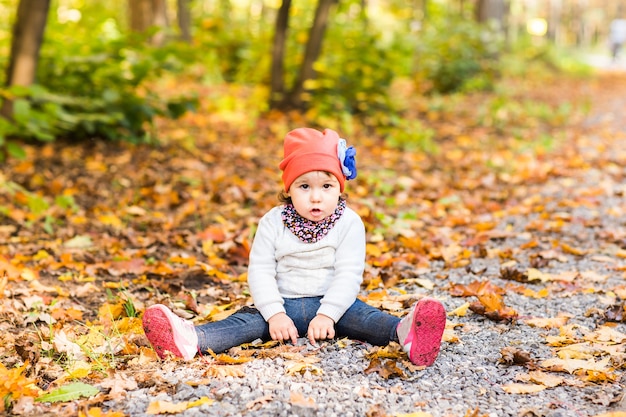 Niña sonriente sentada en el suelo en el parque de otoño al aire libre