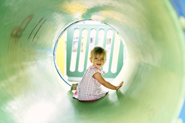 Foto niña sonriente se sienta en un gran tubo en el patio de recreo