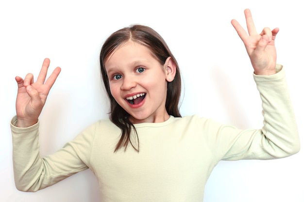 Niña sonriente sobre un fondo claro muestra dos manos signo de paz o victoria