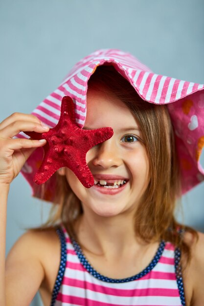 Niña sonriente con sombrero rosa con estrellas de mar. Concepto de vacaciones de verano con retrato de cara de niña hermosa.