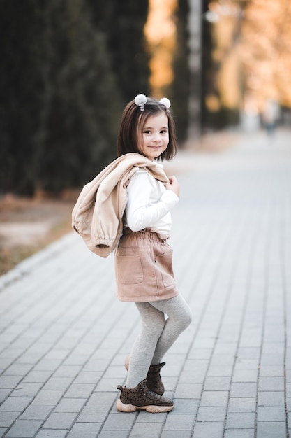 Niña sonriente sosteniendo la chaqueta de pie sobre el fondo de la ciudad