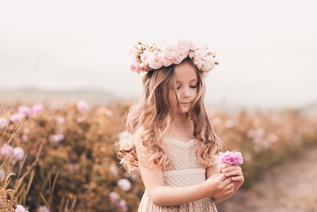 Niña sonriente sosteniendo una flor color de rosa en la pradera al aire libre