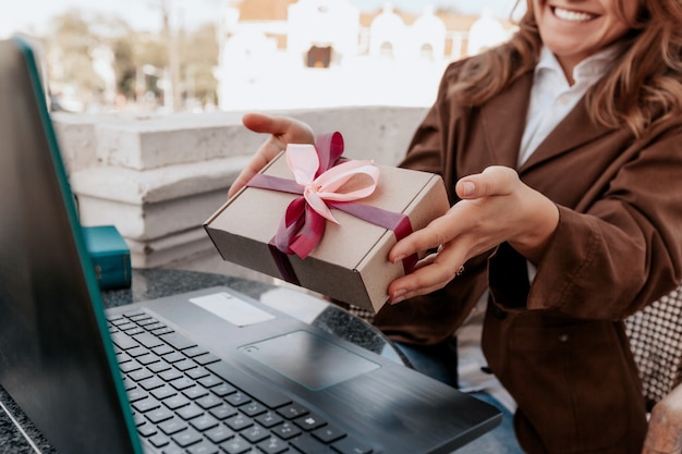 Niña sonriente sosteniendo el regalo de Navidad a su amiga en línea en la computadora portátil