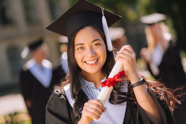 Niña sonriente sosteniendo su diploma con ambas manos orgullosa de su maestría