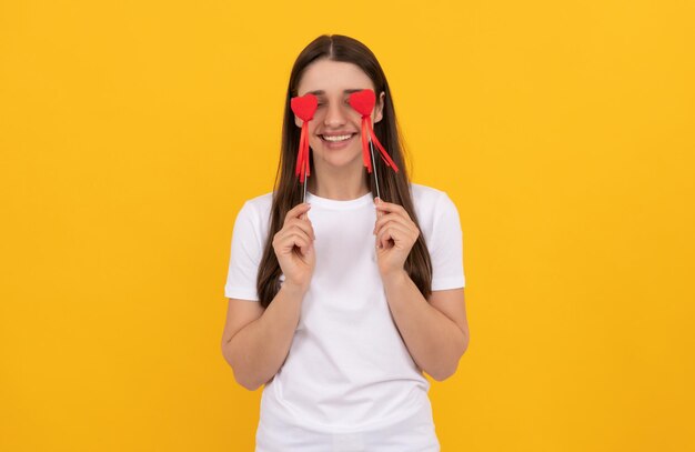 Niña sonriente sostiene corazón en camisa blanca sobre fondo amarillo día de la mujer