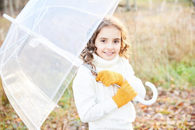 Niña sonriente con un suéter blanco con un paraguas blanco al aire libre en otoño. Foto de alta calidad