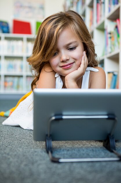 Niña sonriente con tableta digital en la biblioteca de la escuela