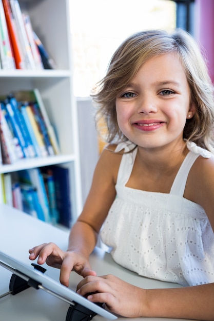 Niña sonriente con tableta digital en la biblioteca de la escuela