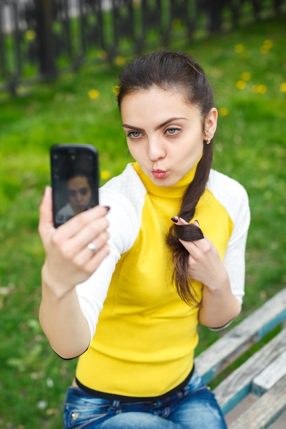 Niña sonriente tomando fotografías con la cámara del teléfono inteligente al aire libre. selfie