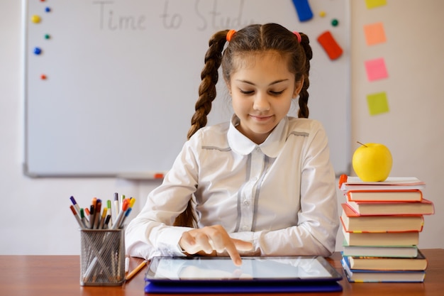 Niña sonriente trabajando en la tableta en el aula