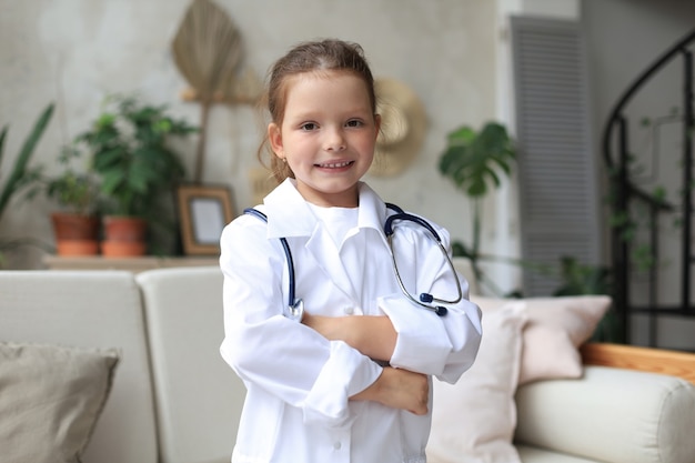 Niña sonriente en uniforme médico jugando con estetoscopio en casa.