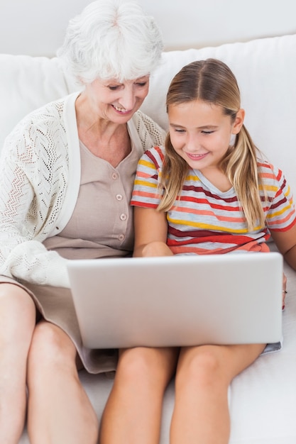 Niña sonriente usando la computadora portátil con la abuela