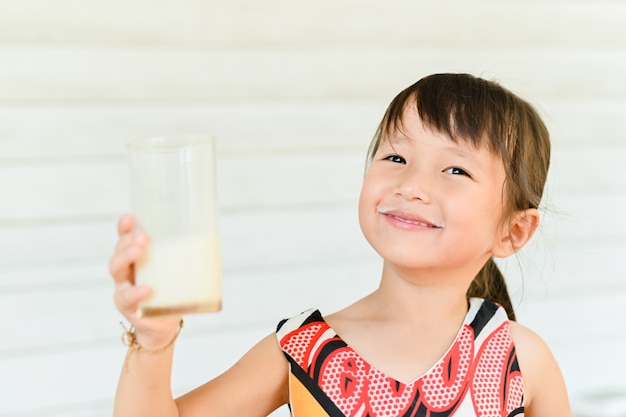 Niña sonriente con un vaso de leche, niña bebiendo leche y dejando un bigote