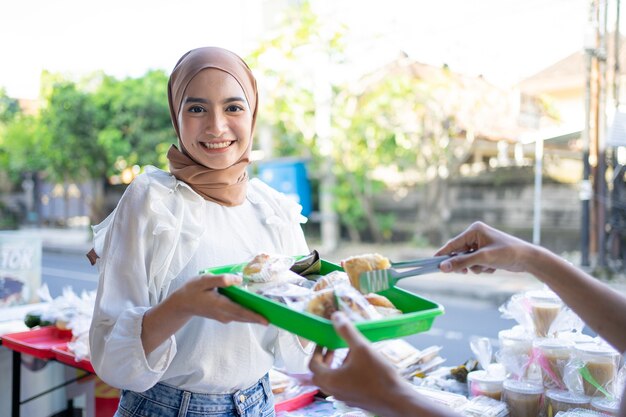 Niña sonriente en un velo dar una bandeja de plástico de comida takjil