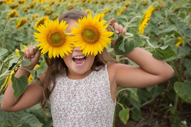 Niña sonriente de verano con dos girasol en sus ojos