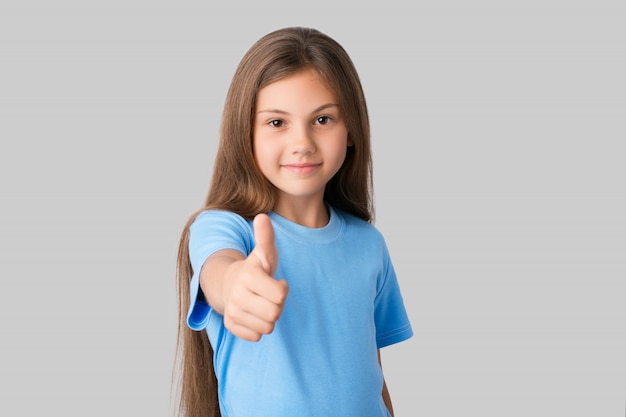 Niña sonriente vestida con camiseta azul mostrando dedo grande