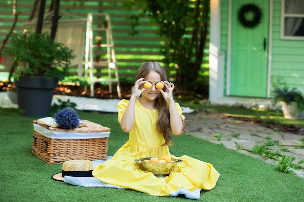 Una niña sonriente con vestido amarillo se entrega a la fruta en el césped verde en verano.