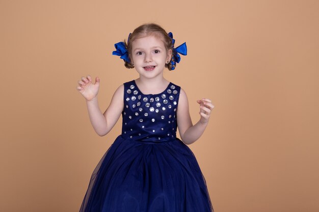 Niña sonriente en vestido azul aislado en pared neutral