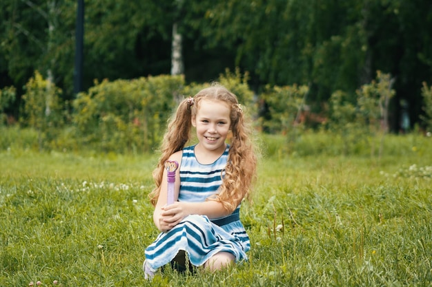Niña sonriente con vestido azul de verano está jugando en el parque, retrato al aire libre