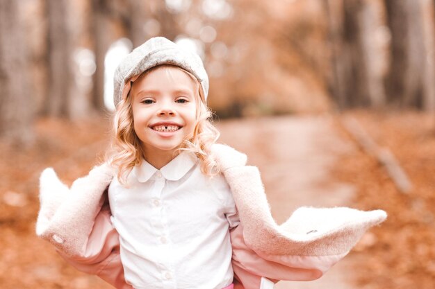 Niña sonriente vistiendo ropa de otoño elegante chaqueta y sombrero al aire libre