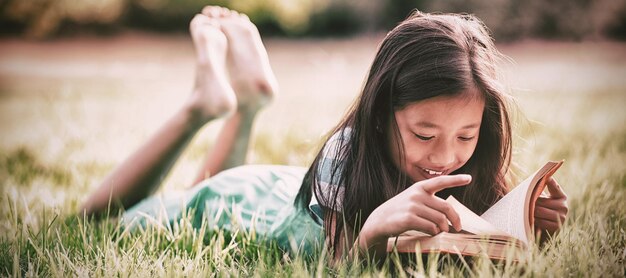 Niña sonriente, yacer césped, y, libro de lectura, en el estacionamiento