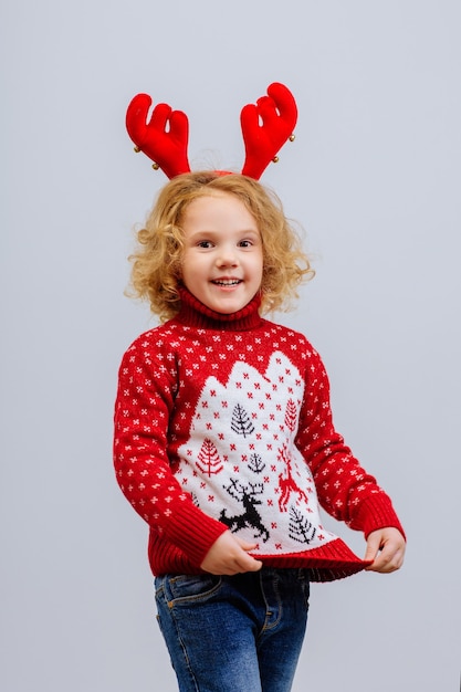 Una niña con una sonrisa en un disfraz de reno de Navidad sobre fondo blanco.