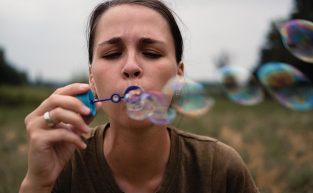 La niña sopla pompas de jabón Una mujer joven se sienta en la naturaleza y sopla bolas de jabón La cara al frente