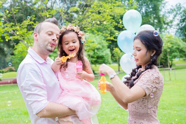 Niña soplando burbujas con su padre y su madre en el parque