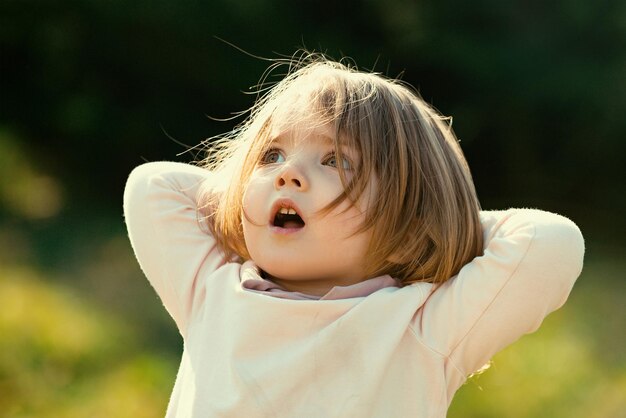 Niña sorprendida en la hierba en el campo en la soleada tarde de verano Cara de bebé emocional